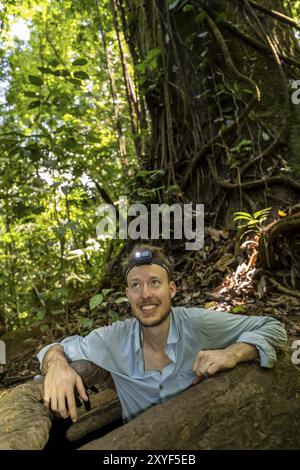 Jeune homme avec lampe frontale, touriste dans la forêt tropicale humide, grimpant de la racine d'un arbre creux, parc national du Corcovado, péninsule d'Osa, Puntarena Banque D'Images