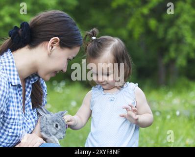 Jolie petite fille et sa mère serrant petit lapin gris. L'amitié et de concept de soins Banque D'Images