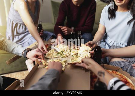 Une fête de pizza, un groupe d'amis discutant et mangeant joyeusement de la pizza à la table et buvant de l'eau gazeuse sucrée. Vue de dessus depuis le deuxième étage. Banque D'Images