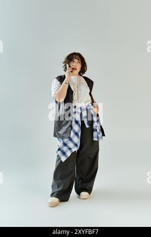 Une femme dans un gilet en cuir élégant, chemise blanche et chemise à carreaux parle au téléphone dans un studio. Banque D'Images