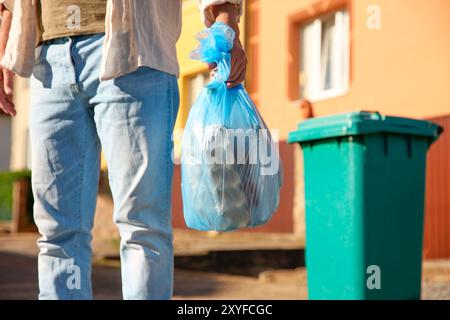 Homme avec sac poubelle plein de déchets et poubelle à l'extérieur, gros plan Banque D'Images