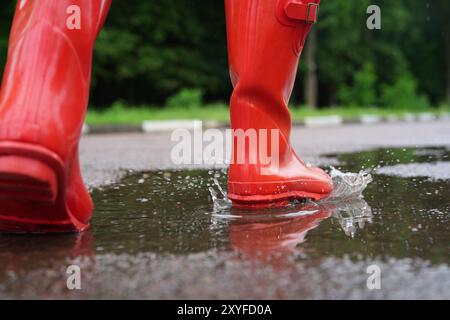 Femme portant des bottes en caoutchouc rouges marchant dans une flaque d'eau à l'extérieur, gros plan Banque D'Images