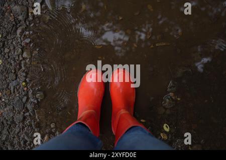 Femme portant des bottes en caoutchouc rouges debout dans une flaque ondulée, vue de dessus Banque D'Images