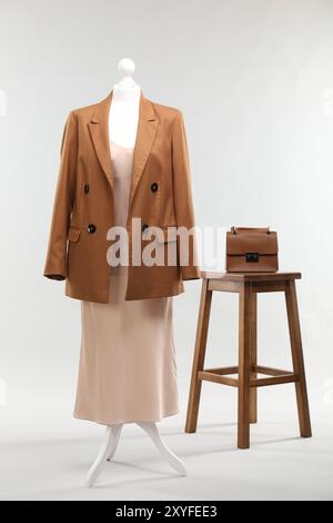 Un mannequin féminin avec robe, veste, tabouret et sac sur fond clair Banque D'Images