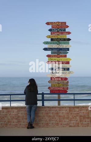 Femme voyageuse près des flèches d'indication vers les villes du monde entier à Torres Vedras, Portugal, Europe Banque D'Images