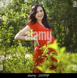 Magnifique Portrait de femme enceinte en robe rouge dans le parc printemps floraison Banque D'Images