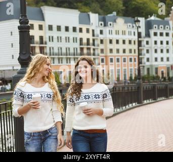 Deux femmes heureux occasionnels ayant une conversation tout en marchant dans la ville avec du café chaud Banque D'Images