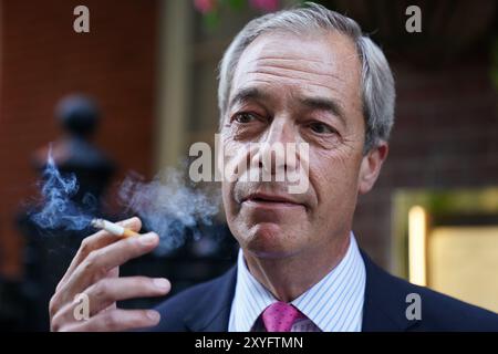 Nigel Farage, leader réformiste britannique, fume devant le pub Westminster Arms à Westminster, Londres. Sir Keir Starmer a déclaré que le gouvernement "prendra des décisions" sur une interdiction potentielle de fumer en plein air dans un effort pour freiner les décès évitables et alléger les pressions sur le NHS. Date de la photo : jeudi 29 août 2024. Banque D'Images