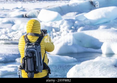 Un homme dans une veste jaune prend une photo d'un lac gelé. La scène est sereine et paisible, avec l'homme capturant la beauté du paysage glacé Banque D'Images