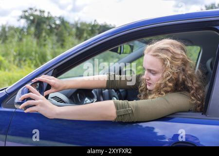 Femme européenne de régler le rétroviseur de voiture bleue dans la nature Banque D'Images