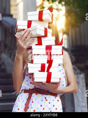 Les boîtes-cadeaux dans les mains du jeune blond woman wearing Polka Dots dress outdoors Banque D'Images