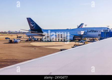 Vue depuis la fenêtre de l'avion du Boeing 747 de Lufthansa stationné sur la piste, avec les passagers embarquant et les bagages chargés. New York. ÉTATS-UNIS. Banque D'Images