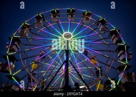 ARLINGTON, Virginie — Une grande roue brillamment éclairée se détache sur le ciel crépusculaire de la foire du comté d'Arlington. Les lumières colorées de la roue créent un spectacle éblouissant, capturant l'atmosphère festive de la foire lorsque le jour se transforme en nuit. Ce carnaval emblématique sert de pièce maîtresse à l'événement communautaire annuel, offrant à la fois des vues palpitantes pour les riders et une scène pittoresque pour les fêtards. Banque D'Images