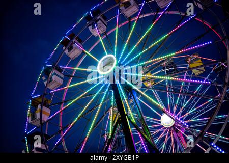 ARLINGTON, Virginie — Une grande roue brillamment éclairée se détache sur le ciel crépusculaire de la foire du comté d'Arlington. Les lumières colorées de la roue créent un spectacle éblouissant, capturant l'atmosphère festive de la foire lorsque le jour se transforme en nuit. Ce carnaval emblématique sert de pièce maîtresse à l'événement communautaire annuel, offrant à la fois des vues palpitantes pour les riders et une scène pittoresque pour les fêtards. Banque D'Images