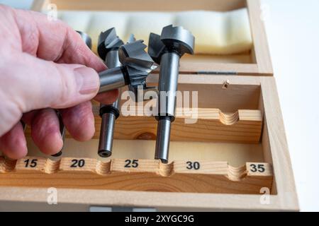 personne tenant l'un d'un ensemble d'embouts de forstner en métal pour l'ingénierie et le travail du bois dans une boîte en bois avec des tailles en métrique Banque D'Images