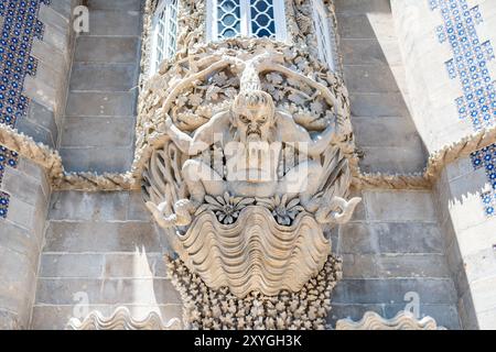 Palais de Pena Statue du Triton Sintra Portugal // SINTRA, Portugal — la statue du Triton à l'entrée du palais de Pena émerge d'un arc, représentant la figure mythologique d'un demi-homme et d'un demi-poisson qui semble soutenir le balcon au-dessus. Créée par le sculpteur portugais António Teixeira Lopes, la statue illustre le style architectural romantiste qui caractérise le palais du XIXe siècle. La figure Triton représente la fusion d'éléments humains et naturels qui est au cœur de la philosophie de conception du Palais de Pena. Le palais, construit dans les années 1840, est l'un des exemples les plus remarquables de romant au Portugal Banque D'Images
