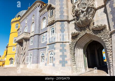 Palais de Pena Statue du Triton Sintra Portugal // SINTRA, Portugal — L'emblématique statue du Triton à l'entrée du palais de Pena. Cette figure mythologique, mi-homme et mi-poisson, émerge d'une arche, semblant soutenir le balcon au-dessus. Créé par le sculpteur portugais António Teixeira Lopes, le Triton est un excellent exemple du style romantiste du palais et symbolise la fusion de l'homme et de la nature au cœur de la philosophie de conception du palais. Banque D'Images