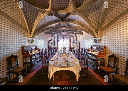 SINTRA, Portugal — la salle à manger du Palais de Pena, anciennement le réfectoire des moines Hiéronymites, convertie par le roi Ferdinand II en salle à manger privée de la famille royale portugaise. La chambre présente des voûtes en côtes manuélines datant du XVIe siècle et est bordée de tuiles du XIXe siècle réalisées par Fábrica Roseira. Le mobilier en chêne, commandé par le roi Ferdinand II en 1866 à Casa Barbosa e Costa, ajoute à l'ambiance historique et royale de l'espace. Banque D'Images