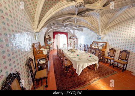 SINTRA, Portugal — la salle à manger du Palais de Pena, anciennement le réfectoire des moines Hiéronymites, convertie par le roi Ferdinand II en salle à manger privée de la famille royale portugaise. La chambre présente des voûtes en côtes manuélines datant du XVIe siècle et est bordée de tuiles du XIXe siècle réalisées par Fábrica Roseira. Le mobilier en chêne, commandé par le roi Ferdinand II en 1866 à Casa Barbosa e Costa, ajoute à l'ambiance historique et royale de l'espace. Banque D'Images