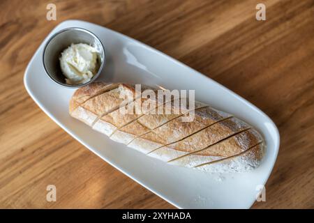 Vue de dessus de baguette de pain avec un côté de beurre sur une assiette blanche plate et table en bois Banque D'Images