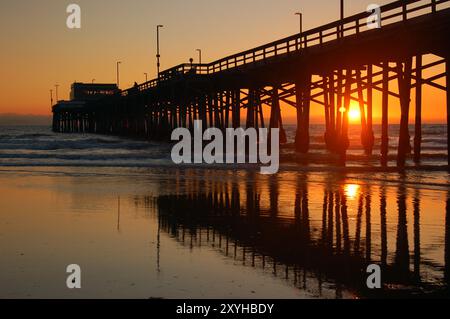 Le soleil se couche sur l'océan Pacifique la jetée de Newport Beach comme les couleurs du ciel se reflètent dans l'eau à marée basse du rivage Banque D'Images