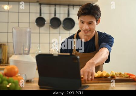 Bel homme adulte faisant un smoothie sain et suivant la recette en ligne sur tablette numérique Banque D'Images