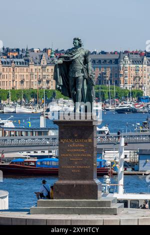 Monument au roi Gustave III de Suède sur Skeppsbron, Gamla Stan, Stockholm, Suède. Vue sur le port et les bâtiments historiques en arrière-plan. Banque D'Images