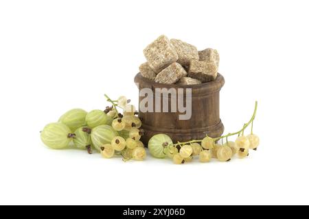 Groseilles à maquereau et raisins de Corinthe jaunes à côté des cubes de sucre de canne dans un bol en bois, isolé sur fond blanc, confiture de baies, préparation de compote Banque D'Images