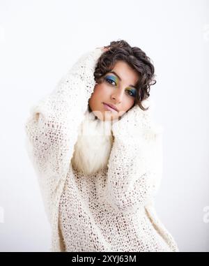 Jolie jeune fille aux cheveux bouclés foncés et maquillage aux couleurs paon porte un pull blanc Banque D'Images