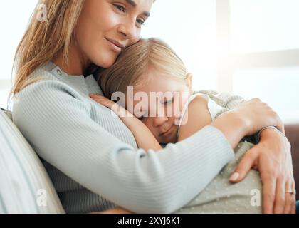 Mère, fille et câlin pour le confort à la maison, enfant console et soutien ou soin pour enfant triste sur le canapé. Maman, fille et embrasser pour la sécurité dans Banque D'Images