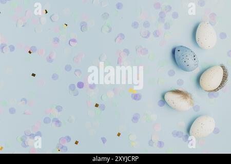 Happy Easter holiday, coming spring concept. Flat lay with white, colorful quail eggs, feather. Blue table background, paper confetti, copy space for Stock Photo