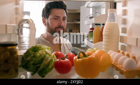 Point de vue POV à l'intérieur du réfrigérateur homme caucasien mari homme Guy propriétaire chef ouvert réfrigérateur plein de légumes frais sains vérifier les ingrédients Banque D'Images