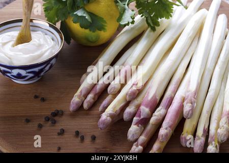 Asperges pelées et ingrédients pour une sauce sur planche de bois Banque D'Images