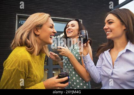 Trois jeunes femmes heureuses riant, buvant du vin rouge, s'amusant. Concept de fête et d'amitié Banque D'Images