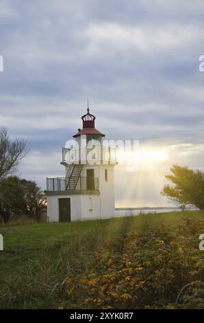 Phare, Spodsbjerg FYR à Huntsted sur la côte du Danemark. Rayons de soleil qui brillent à travers les nuages. Prairie avec arbres. Paysage photo de la mer Banque D'Images