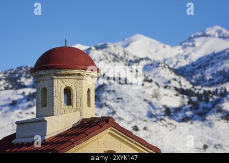 Gros plan d'une tour d'église avec un toit rouge dans les montagnes enneigées sous un ciel clair, Lefka Ori, montagnes blanches, massif montagneux, ouest, Crète, Grèce, Banque D'Images