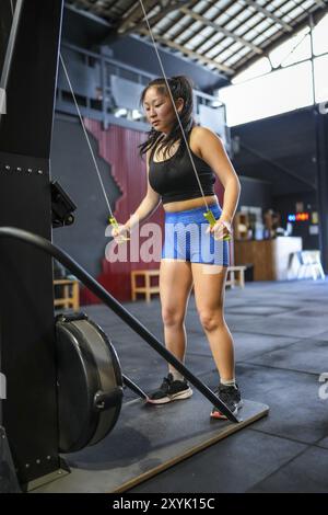 Photo verticale d'une forte femme chinoise exerçant avec des poids dans une machine à tirer lat Banque D'Images