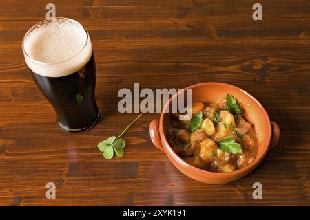 Ragoût irlandais traditionnel sur un bol brun avec une pinte de bière forte et un trèfle sur une table Banque D'Images