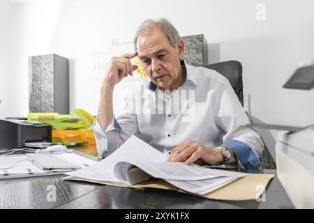Homme âgé dans une chemise blanche assis à un bureau et feuillette à travers un dossier de document Banque D'Images
