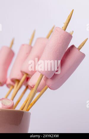 Une image verticale avec des brochettes avec des guimauves sur le côté gauche, sur un fond blanc. La photo souligne les guimauves prêtes pour t Banque D'Images