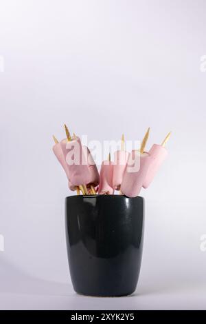 Image verticale montrant des brochettes de guimauve prêtes à être rôties, placées dans une tasse grise. Le focus se trouve sur le côté gauche de l'arrière-plan blanc, en surbrillance Banque D'Images