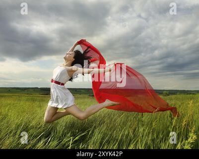 Brunette fille sautant avec un tissu rouge dans la journée d'été. Potrrait extérieur Banque D'Images