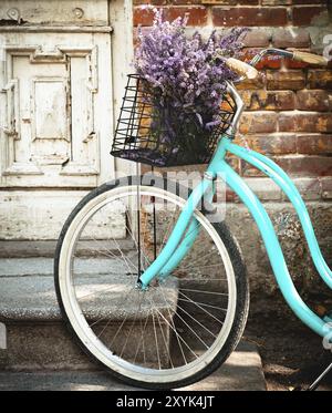 Vintage bycycle avec panier avec des fleurs de lavande près de la vieille porte en bois Banque D'Images