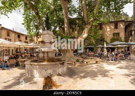 Les gens au café en plein air sur la place du village de la liberté, St Guilhem le désert, Hérault, Occitanie, France, Europe Banque D'Images