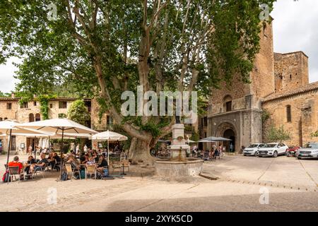 Les gens au café en plein air sur la place du village de la liberté, St Guilhem le désert, Hérault, Occitanie, France, Europe Banque D'Images