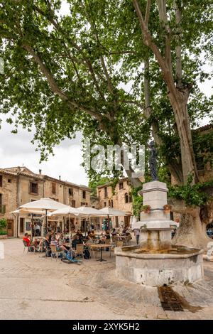 Les gens au café en plein air sur la place du village de la liberté, St Guilhem le désert, Hérault, Occitanie, France, Europe Banque D'Images