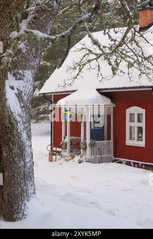 Maison suédoise en bois peint en rouge typique dans un paysage hivernal avec un traîneau devant la maison et un drapeau suédois suspendu au-dessus de l'entrée. Red painte Banque D'Images