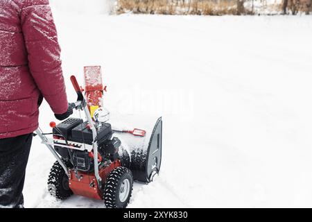 Détail de la souffleuse à neige rouge portable alimentée par l'essence en action. Homme à l'extérieur utilisant une souffleuse à neige après une tempête de neige. Déneigement, assistance pour fraise Banque D'Images
