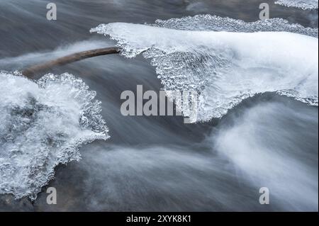 Longue exposition dans le courant d'un ruisseau à partir d'une branche entre deux roches recouvertes de glace Banque D'Images