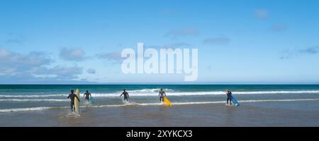 Une image panoramique de surfeurs passionnés qui courent dans la mer à la maison du surf britannique, Fistral Beach à Newquay en Cornouailles au Royaume-Uni. Banque D'Images